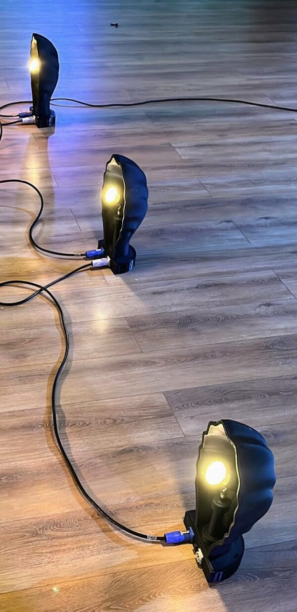 3x Black scallop shell footlights shown on a wooden dance floor with powercon cables between them